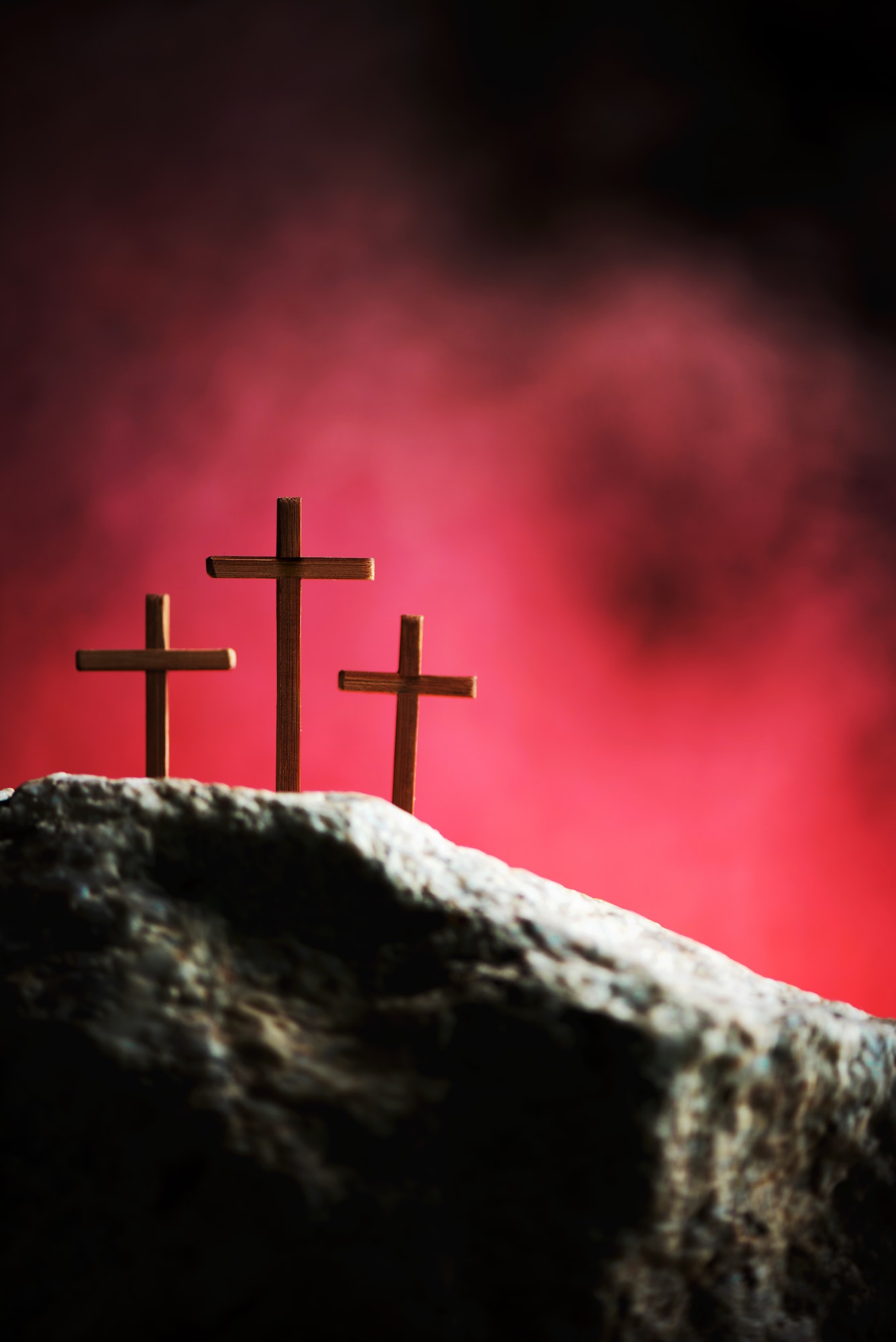Crucifixion, resurrection of Jesus Christ. Three crosses against red sky on Calvary hill background